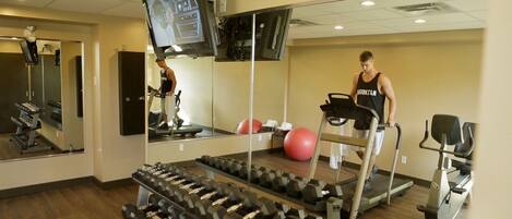 Une salle de sport équipée de tapis de course, d’un miroir, d’un téléviseur et d’un porte-poids.