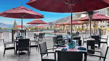 Un espace de restauration en plein air avec des parasols rouges, des chaises en osier noir et des tables dressées pour le repas.