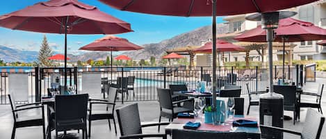 An outdoor dining area with red umbrellas, black wicker chairs, and tables set for dining.