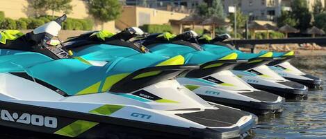 Eine Reihe von Jet-Skis mit dem Schriftzug "GTI", geparkt am Ufer, mit Häusern im Hintergrund.