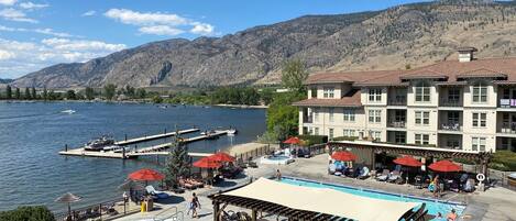A hotel with a pool, outdoor seating, and a view of a lake and mountains.