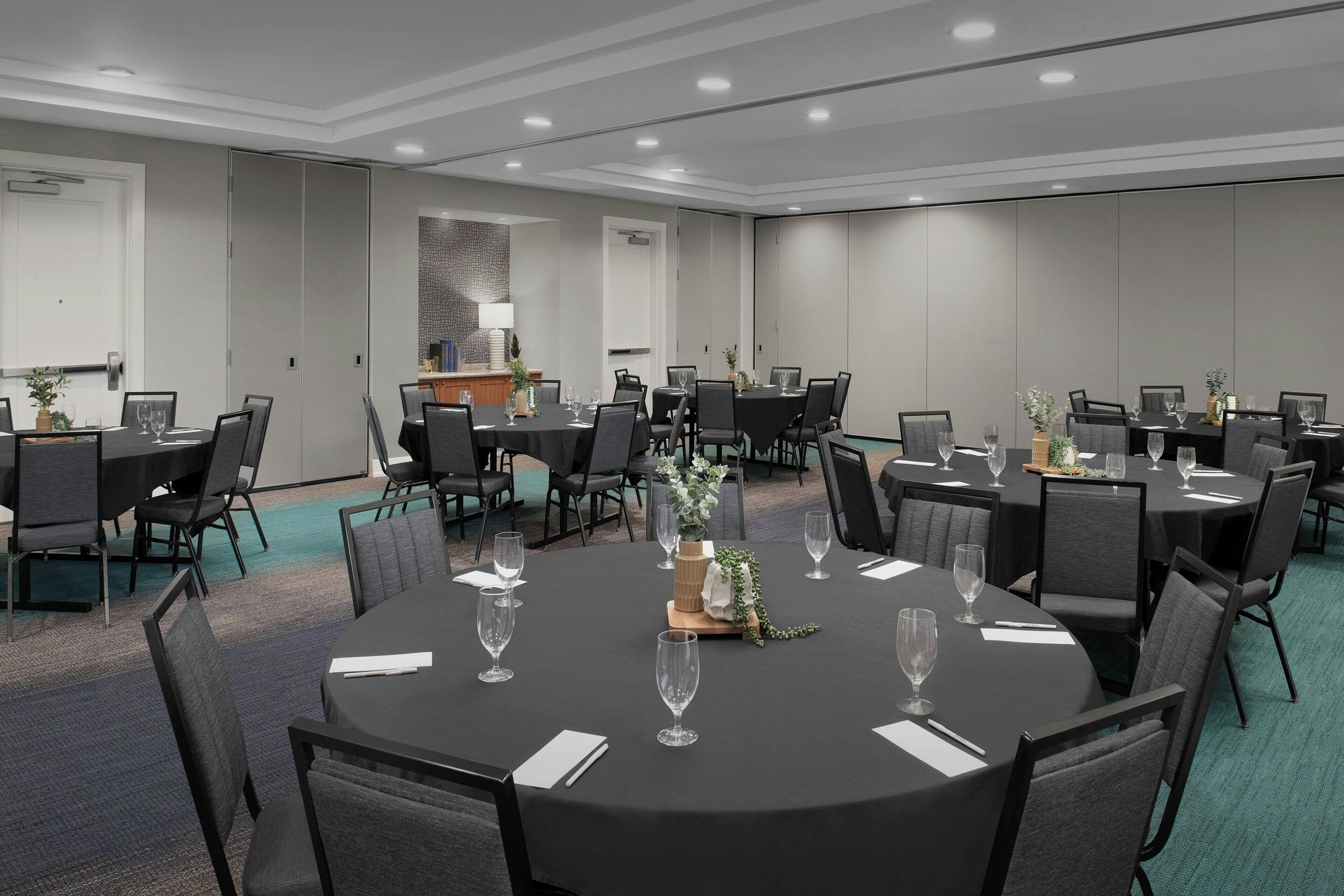 A conference room with multiple tables and chairs, equipped with glassware and centerpieces.