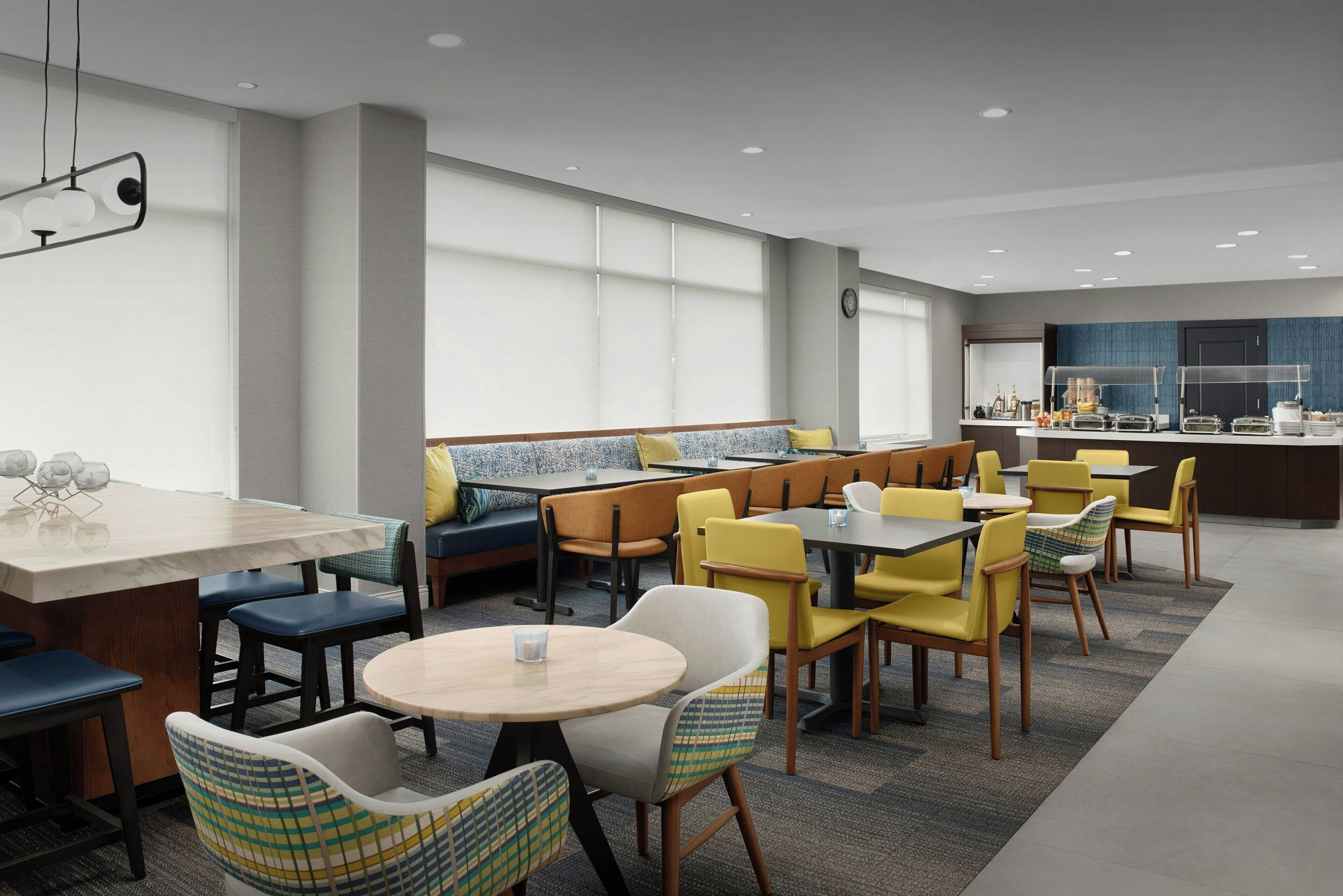 Een moderne eethoek met een combinatie van zitbanken en tafels, een keukenbar en een groot raam dat voor natuurlijk licht zorgt.