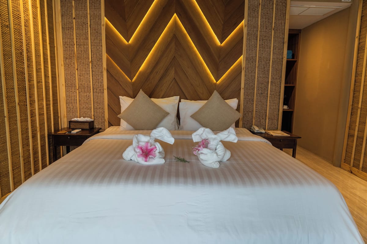 A hotel room with a large bed, two nightstands, a wooden headboard with a chevron pattern, and a small shelf with a telephone and papers.