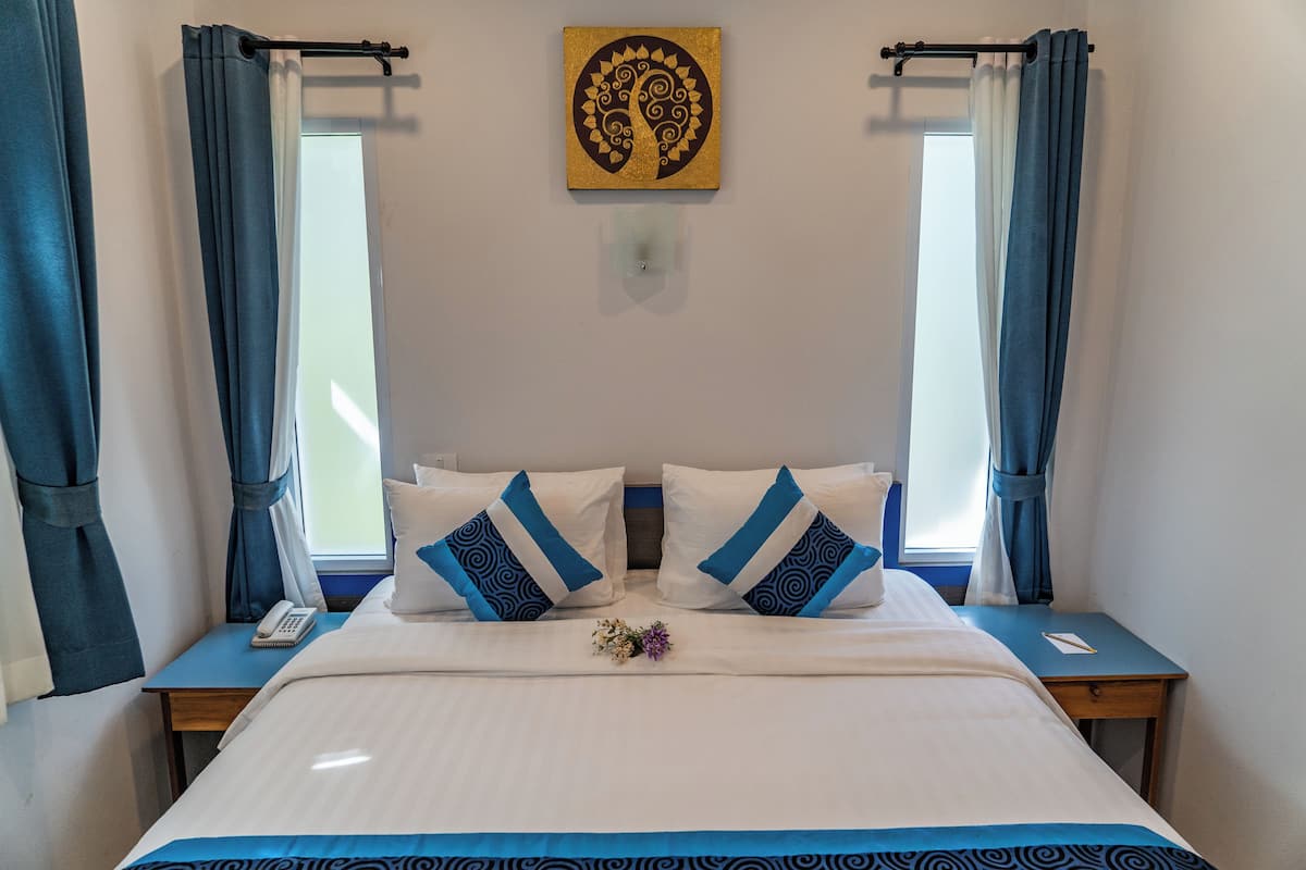 A hotel room with a large bed, two bedside tables, a nightstand, a wall-mounted artwork, and a window with curtains.