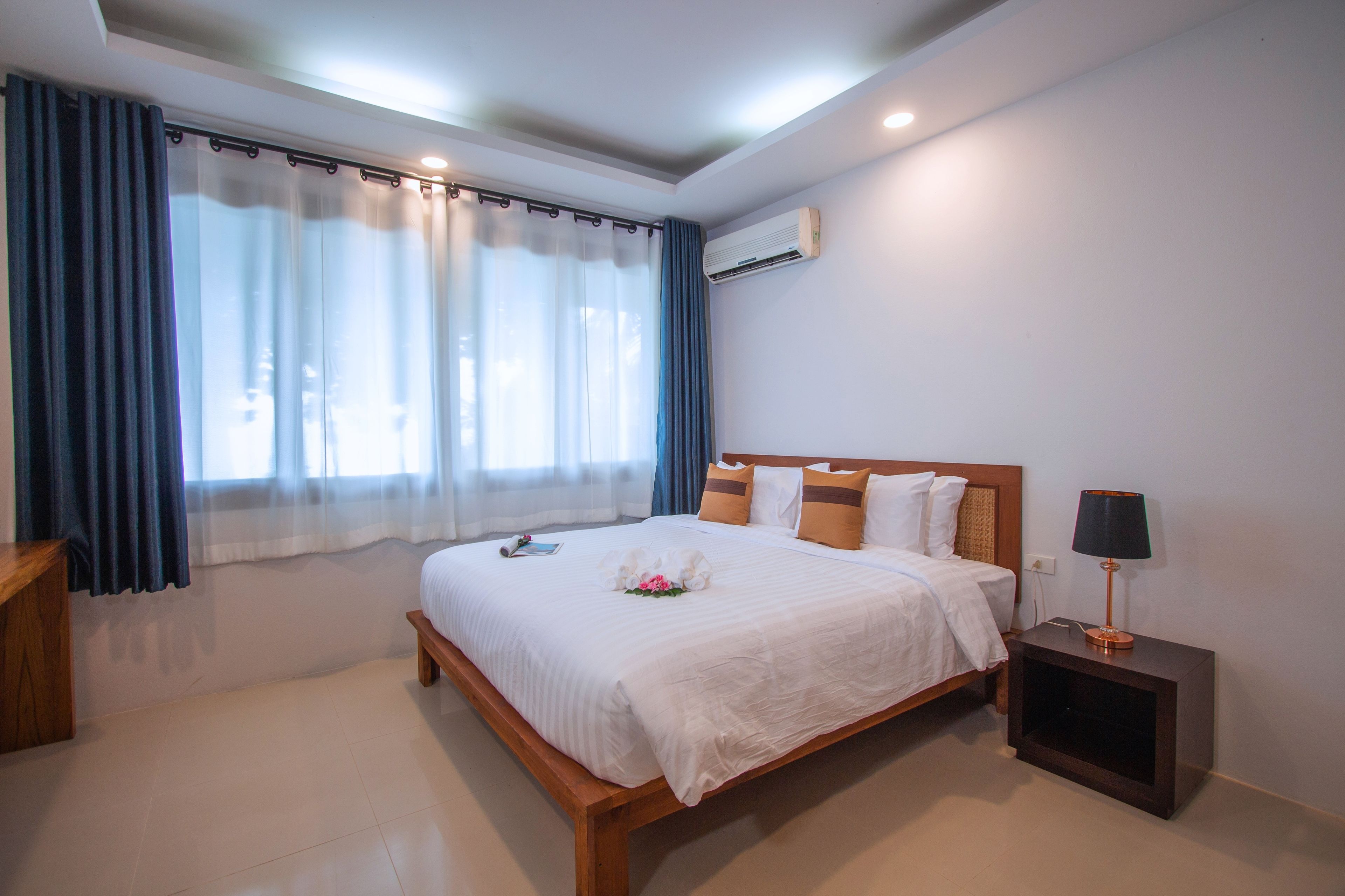 Una habitación de hotel con una cama grande, una mesita de noche con lámpara y una ventana con cortinas.