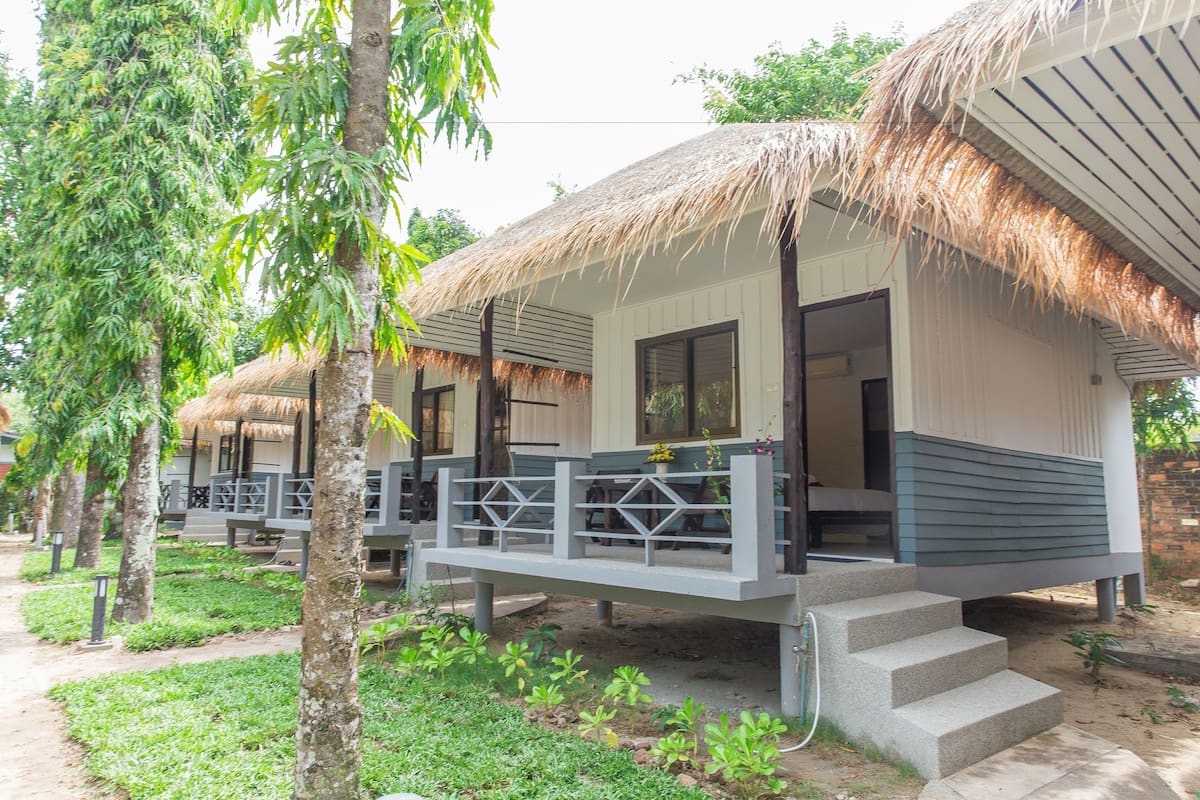 A row of thatched-roof cottages with outdoor seating, surrounded by greenery.