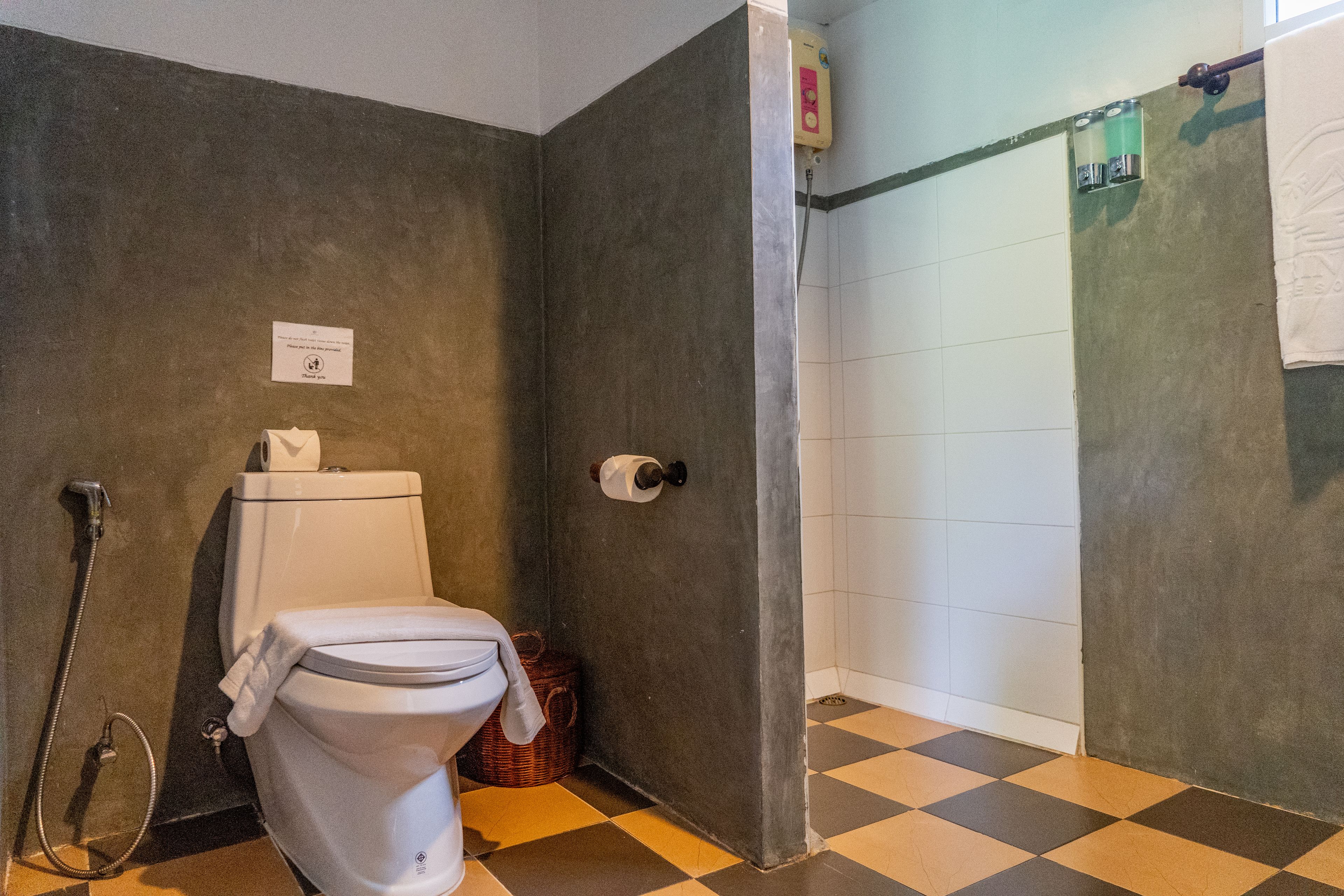 A bathroom with a toilet, a shower, and a checkered floor.