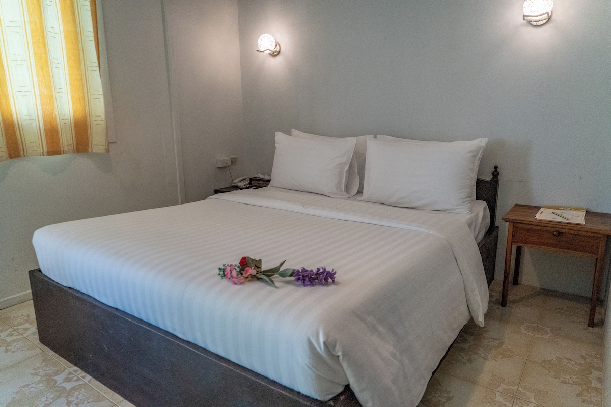 A neatly made bed with white linens and a floral arrangement on the bed.