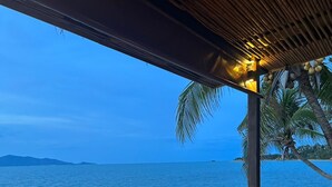 A dining area with tables set for two, overlooking a body of water with a view of distant islands. - Adarin Beach Resort (Koh Samui)