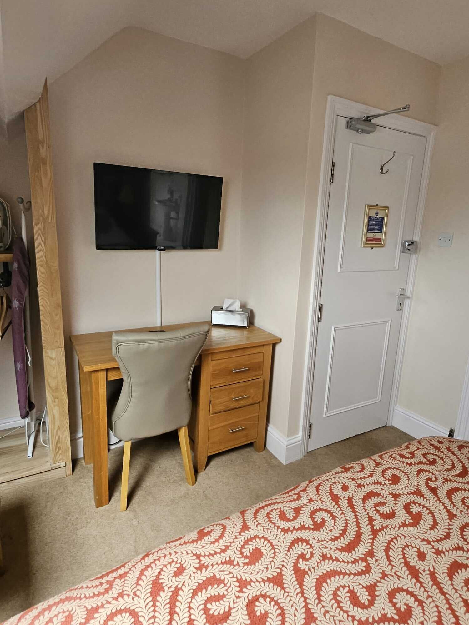A bedroom with a bed, a desk, a chair, a television, and a door.