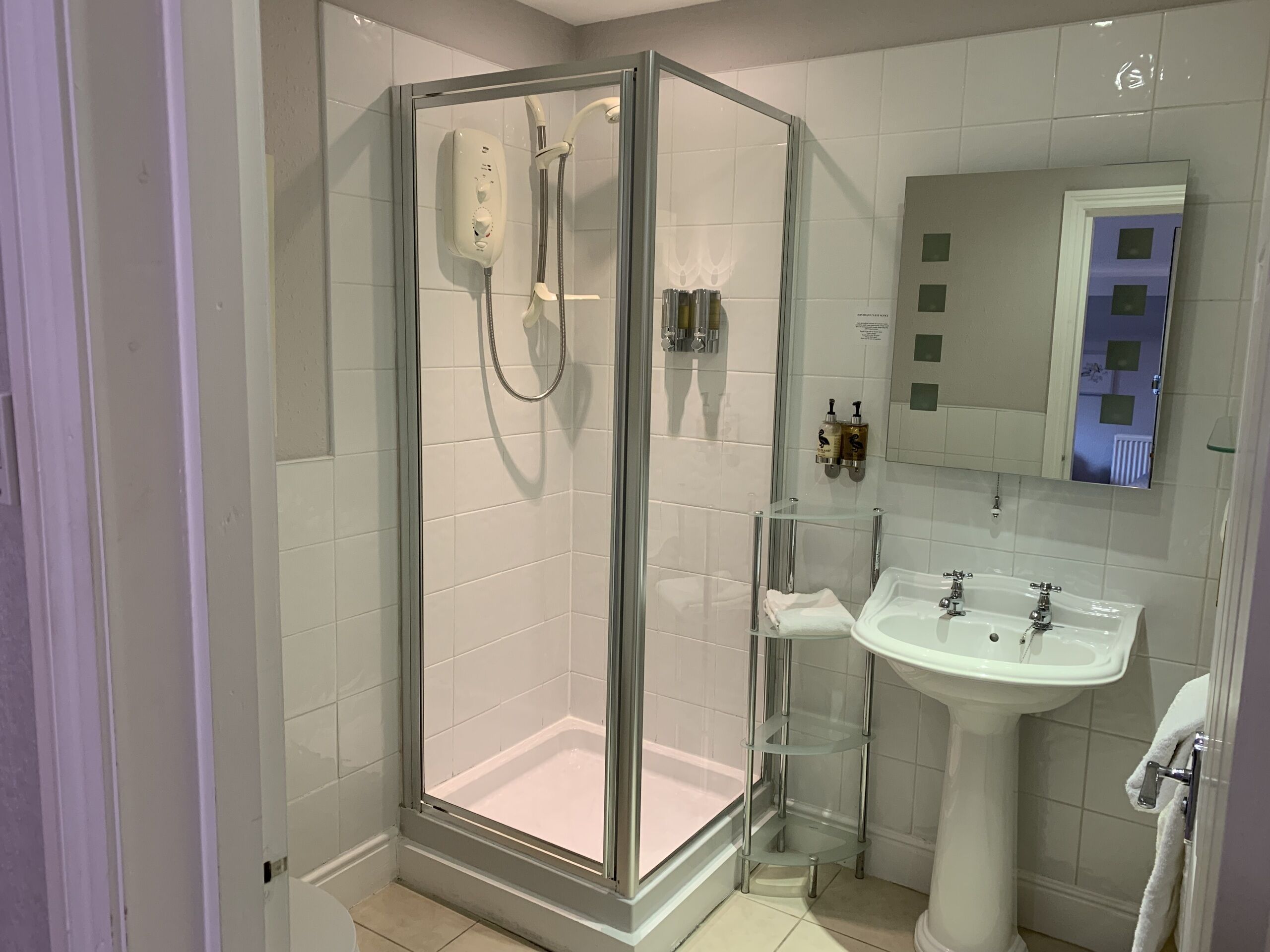 Un baño moderno con ducha envuelta en vidrio, lavamanos pedestal y espejo sobre él.