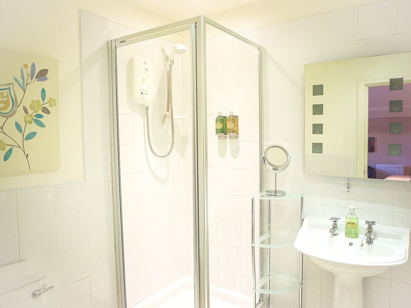 A modern bathroom with a glass-enclosed shower, a white sink with a mirror, and a decorative wall piece.