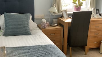 A neatly arranged bedroom with a bed, bedside table, desk, and chair.
