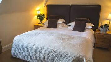 A neatly made bed with a white quilt and two dark brown pillows, flanked by two bedside tables with lamps and a vase of flowers.