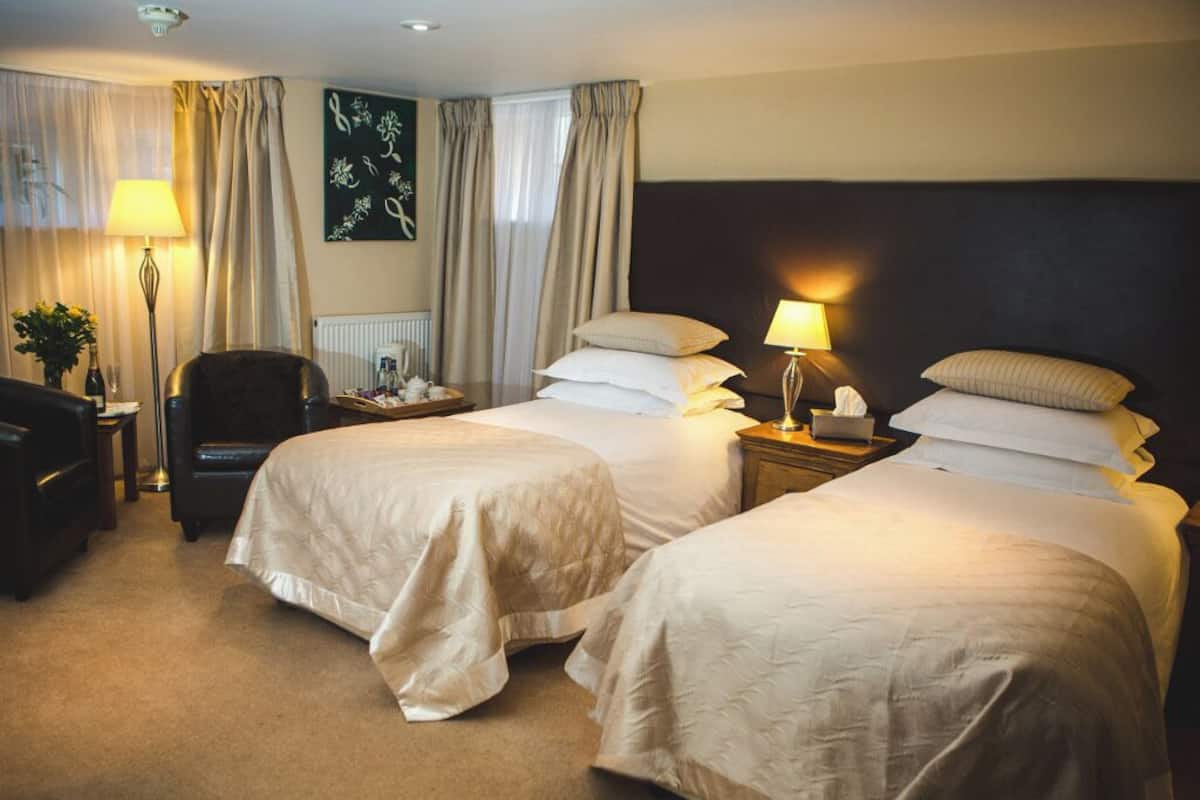 A hotel room with two beds, a desk, a chair, a lamp, and a radiator.