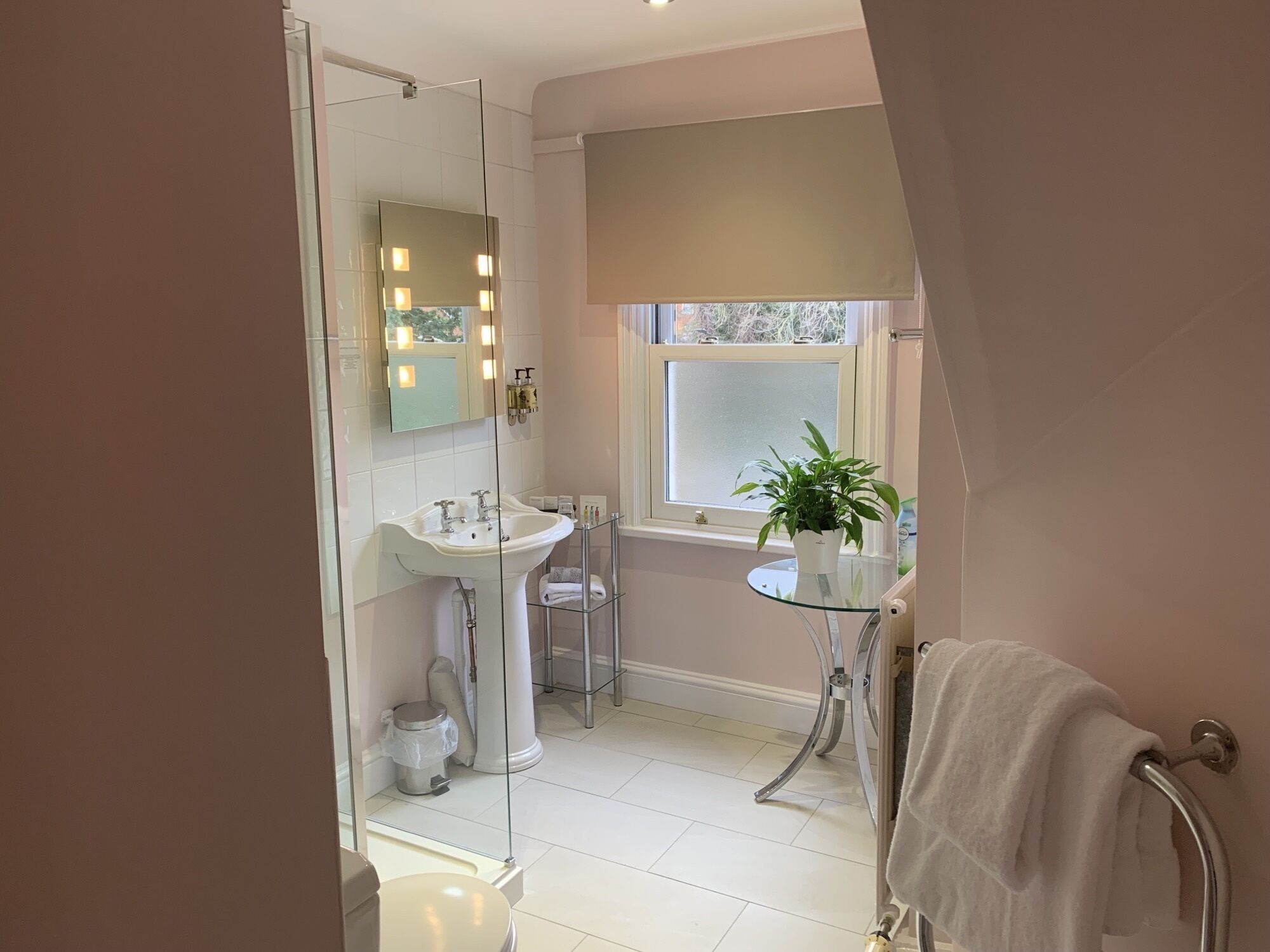 A modern bathroom with a glass shower enclosure, a pedestal sink, and a window with a view.