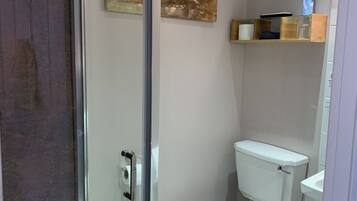 Ett modernt badrum med en dusch som är avskärmad med glasväggar, en toalett och ett handfat. Det finns två tavlor som hänger på väggen och en hylla med toalettartiklar.