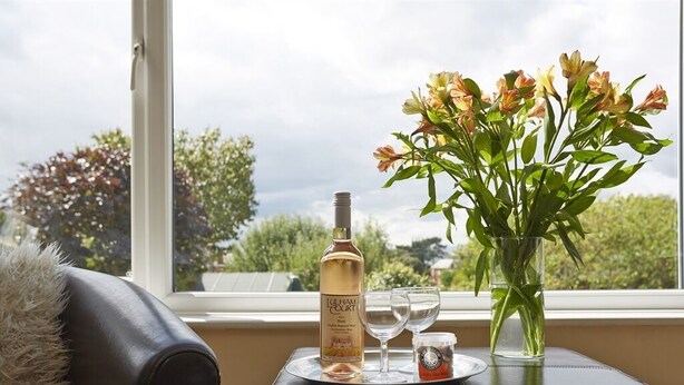 A table with a bottle of liquor, a glass, and a vase of flowers by a window. - Somerville House (Hereford)