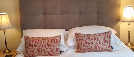 A hotel room with a bed, two bedside lamps, a headboard, and a painting on the wall.