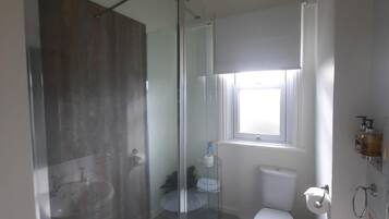 Un baño moderno con mampara de vidrio, inodoro y lavamanos.
