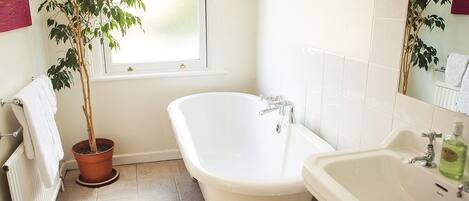 A bathroom with a freestanding bathtub, a sink, and a potted plant.