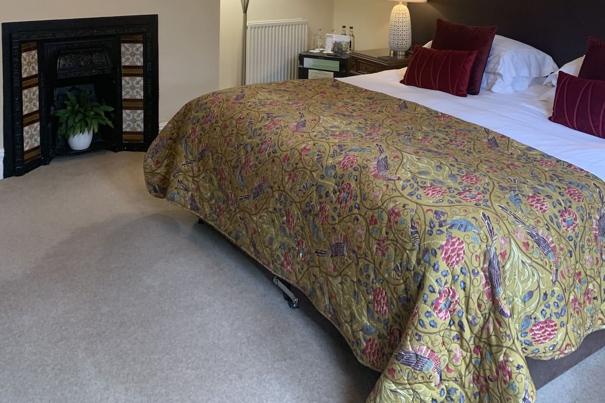 A hotel room with a large bed, two bedside lamps, a fireplace, and a floral artwork on the wall.