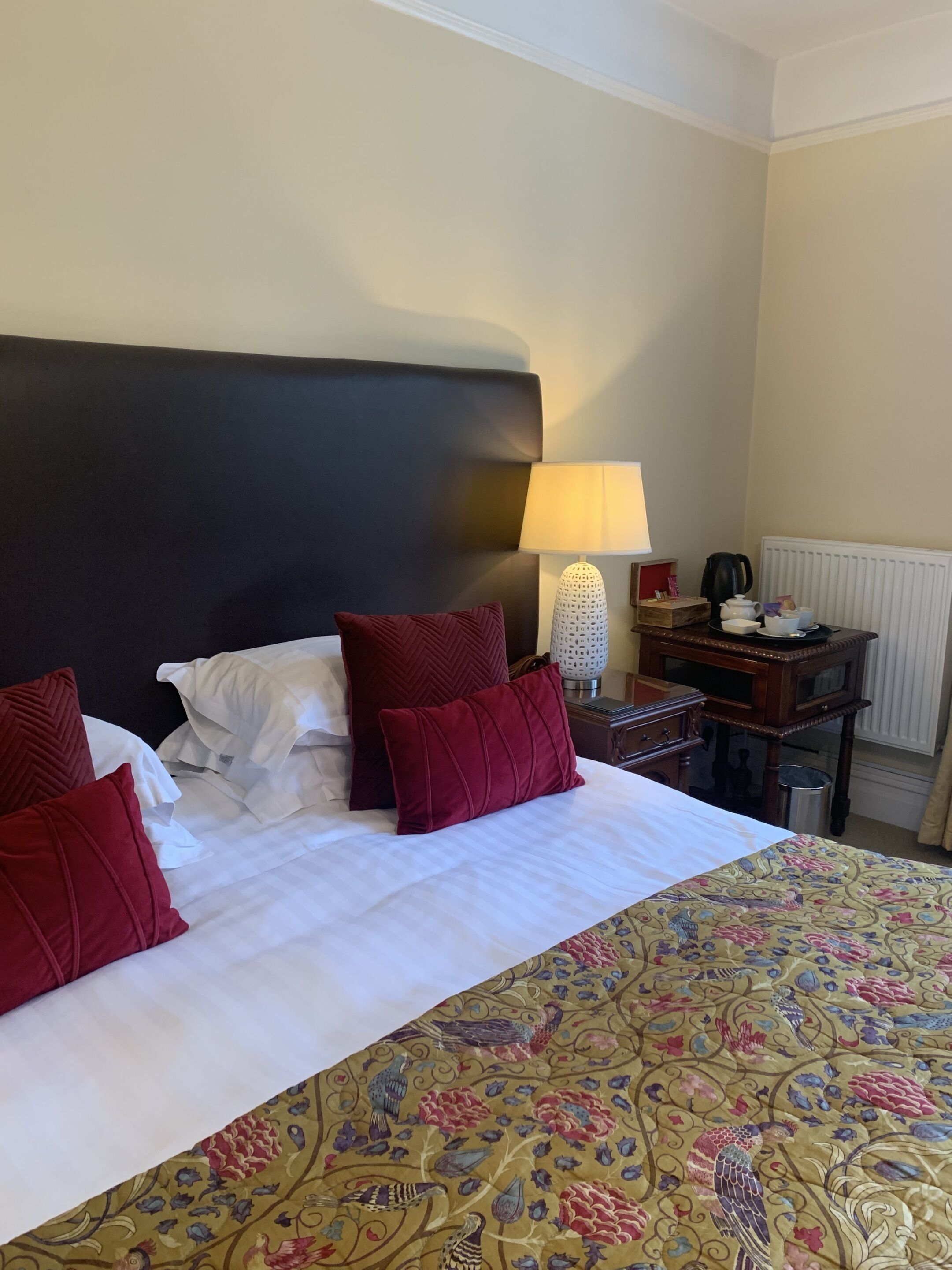 A hotel room with a large bed, a nightstand, a lamp, and a radiator.