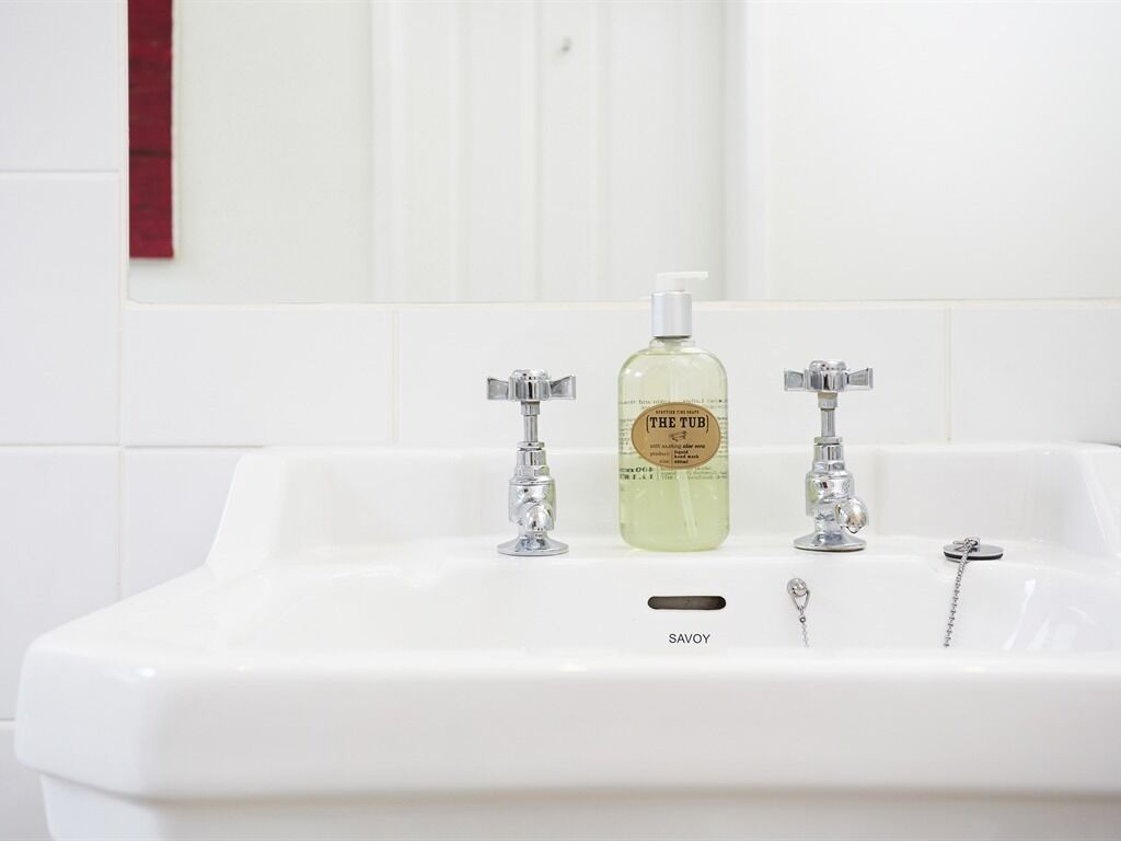A white bathroom sink with two faucets and a bottle of Savoy soap.