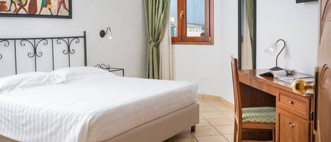Une chambre à coucher avec un lit, un bureau, une chaise, une fenêtre et un tableau accroché au mur.