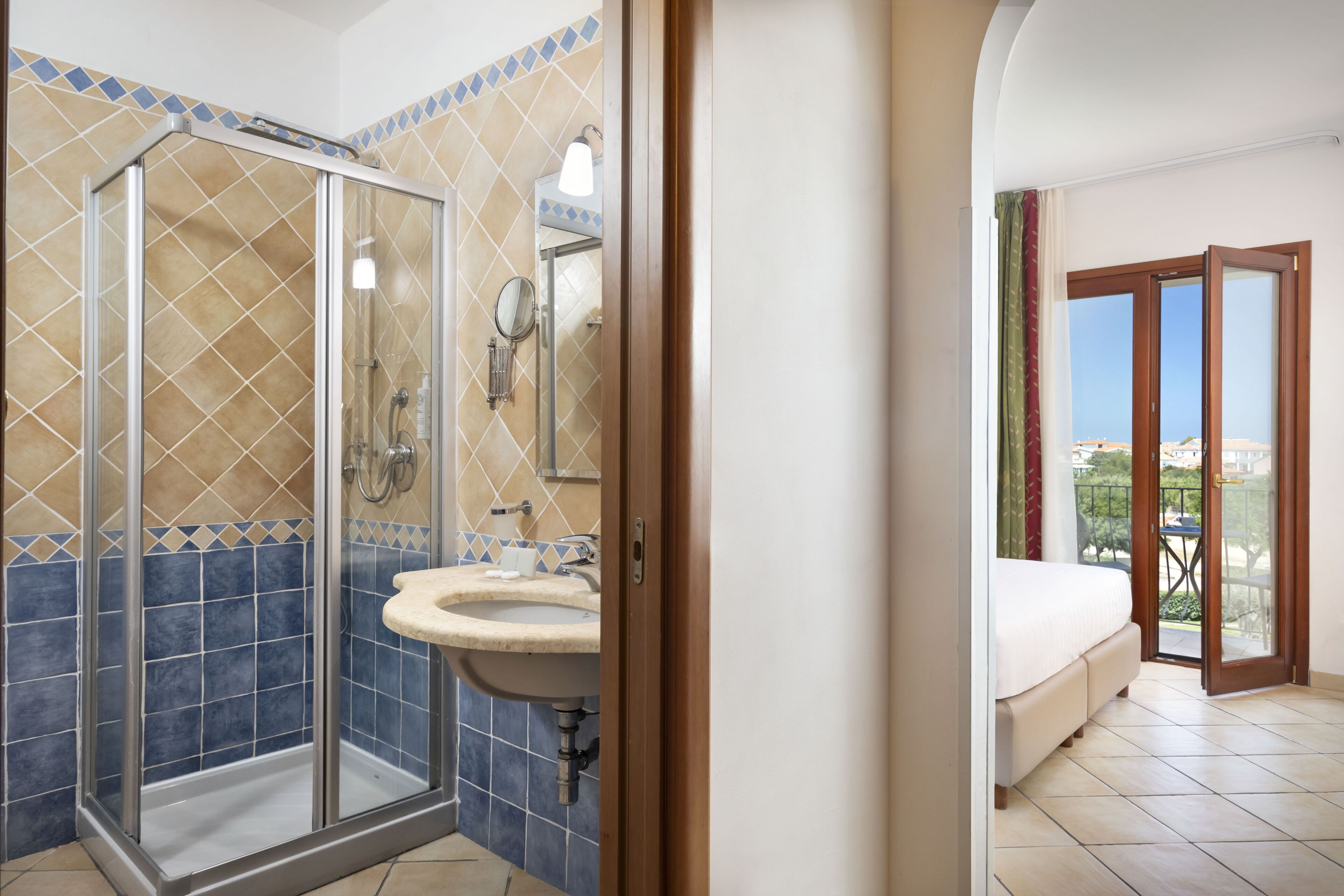 Un bagno con box doccia in vetro, un lavandino e uno specchio. Si vede un letto con vista sull'esterno attraverso una porta scorrevole.