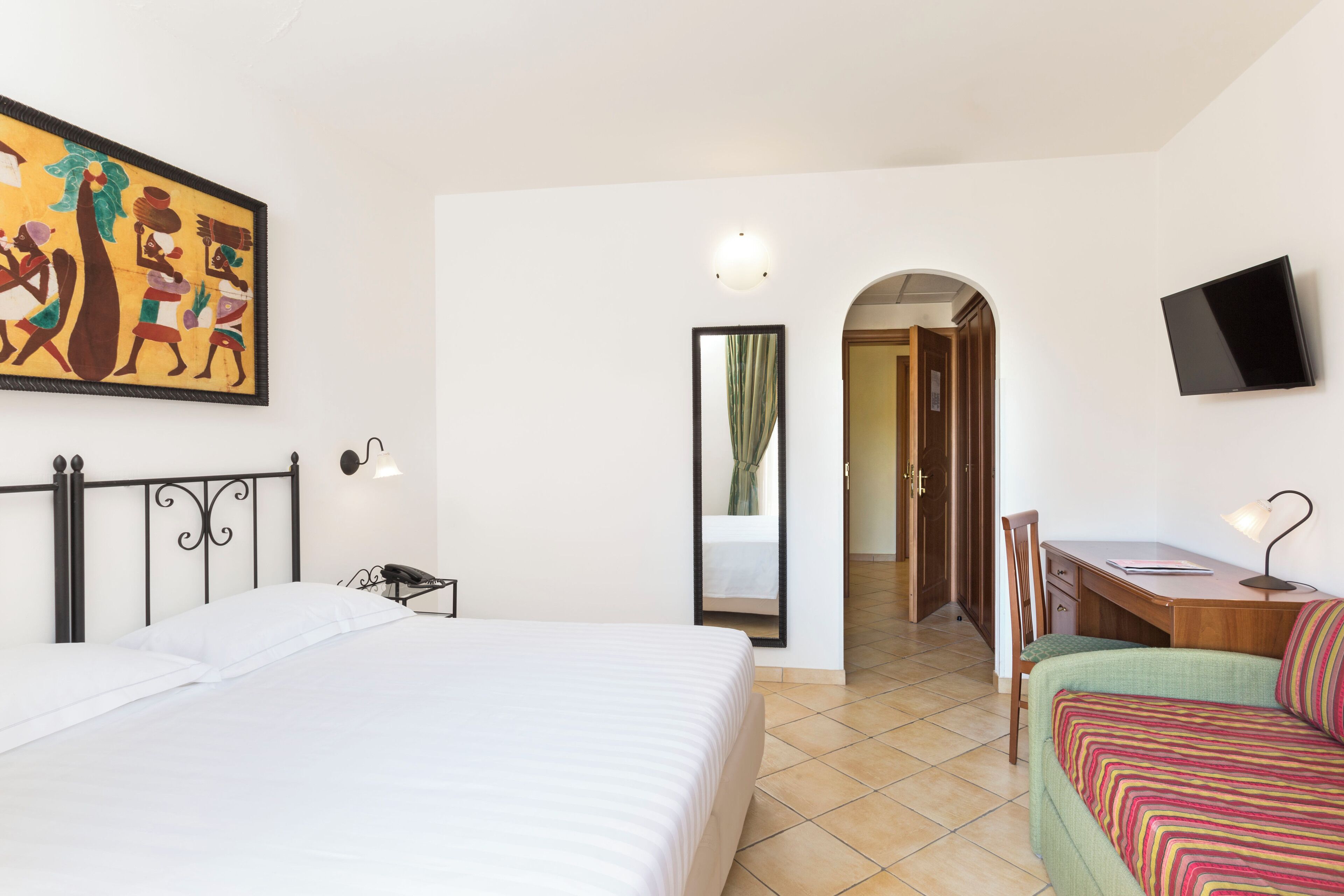 Une chambre d’hôtel avec un lit, un bureau, une chaise, une télévision et un tableau au mur.