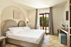 Habitación de hotel con una cama grande, un escritorio con silla, una mesita, una planta en maceta y vistas al exterior.