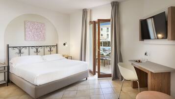 Habitación de hotel con cama, escritorio, silla, televisor y balcón con vistas a edificios.