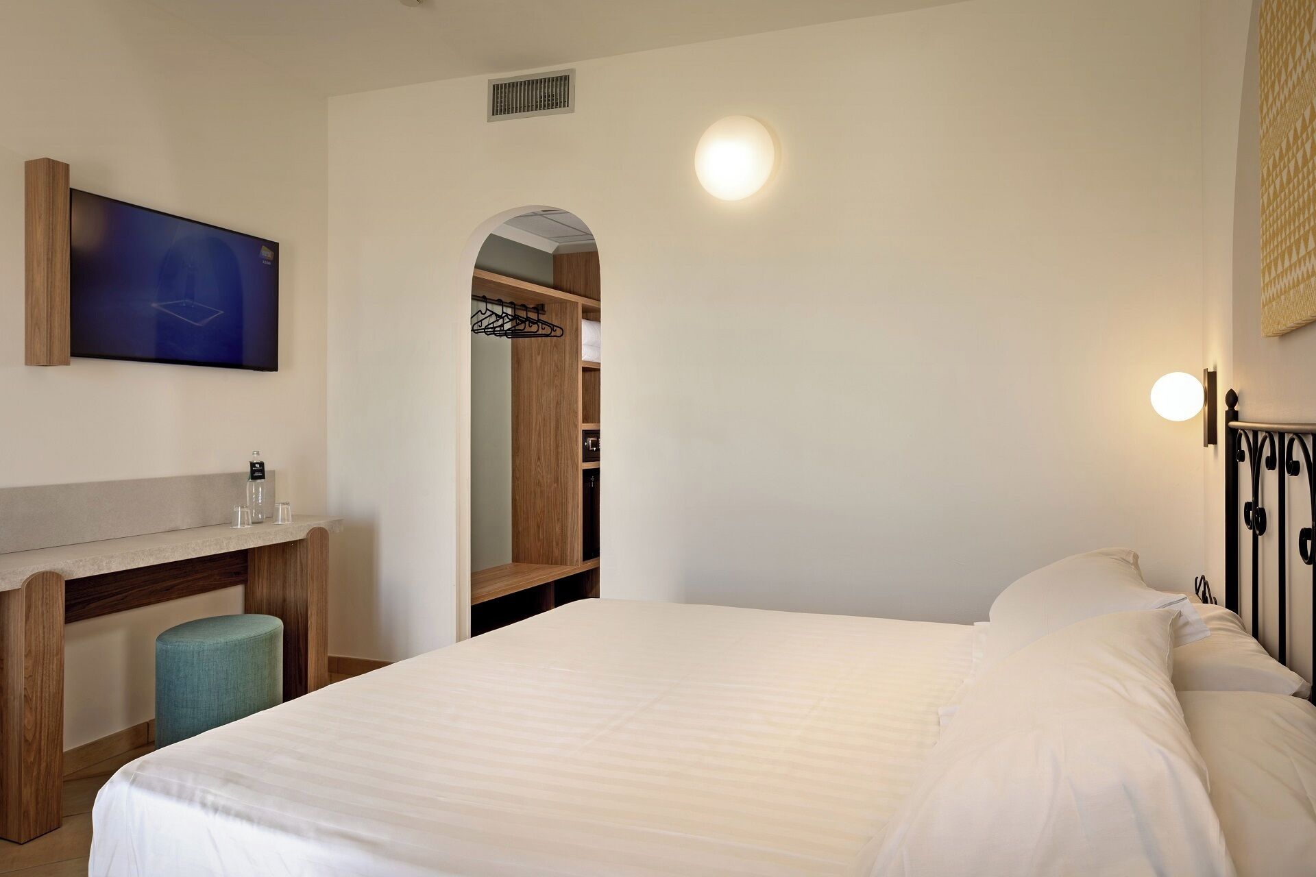 Ein Schlafzimmer mit einem Bett, einem Schreibtisch mit Stuhl, einem Kleiderschrank und einem an der Wand befestigten Fernseher.