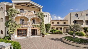A multi-story building with a stone facade, arched balconies, and a courtyard with a central tree.