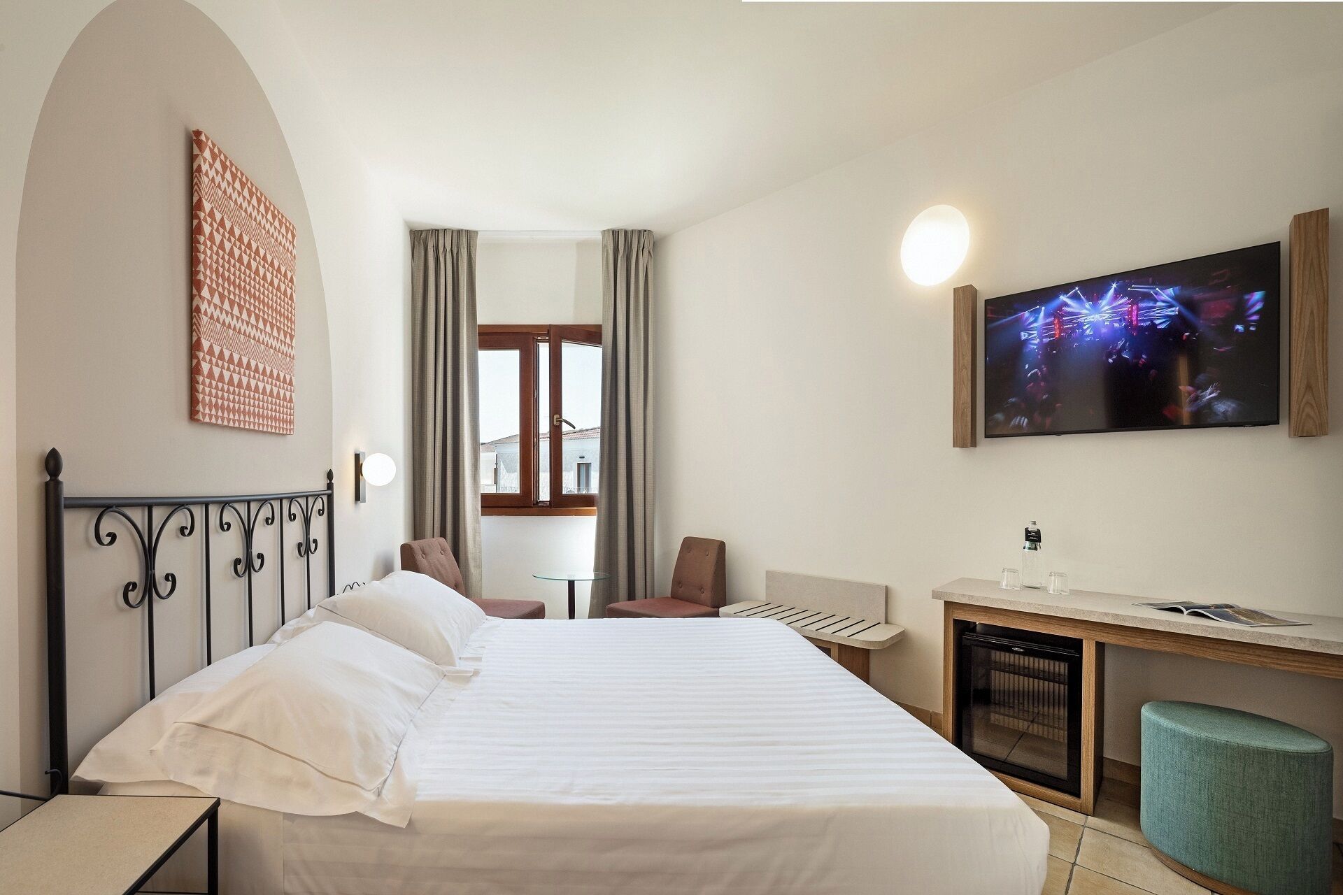 Une chambre d’hôtel avec un lit, un bureau avec un ordinateur, une télévision et une fenêtre avec des rideaux.