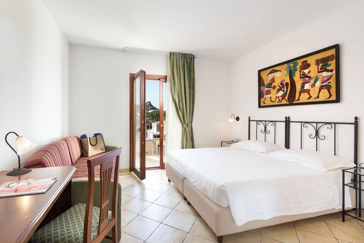 Ein Hotelzimmer mit einem Bett, einem Schreibtisch mit Lampe, einem Sessel und einer Couch, sowie einem Bild an der Wand.