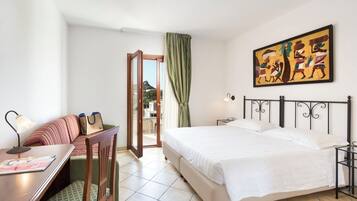 Una habitación de hotel con cama, escritorio con lámpara, silla, sofá y un cuadro en la pared.