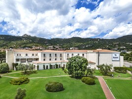 A hotel with a courtyard, surrounded by greenery and a mountainous backdrop.