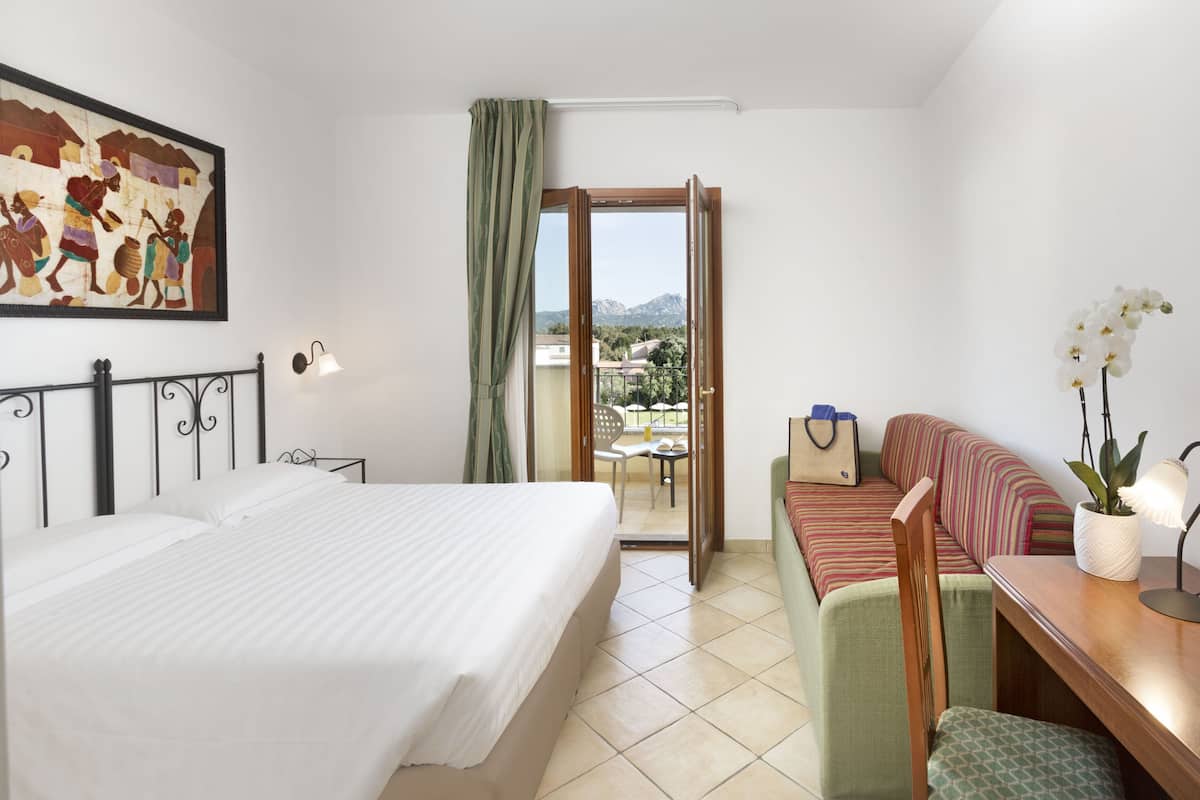 Ein Hotelzimmer mit Bett, Sofa, Schreibtisch und einem Balkon mit Bergblick.