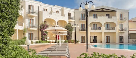 A hotel courtyard with a swimming pool, outdoor seating, and a building with balconies.