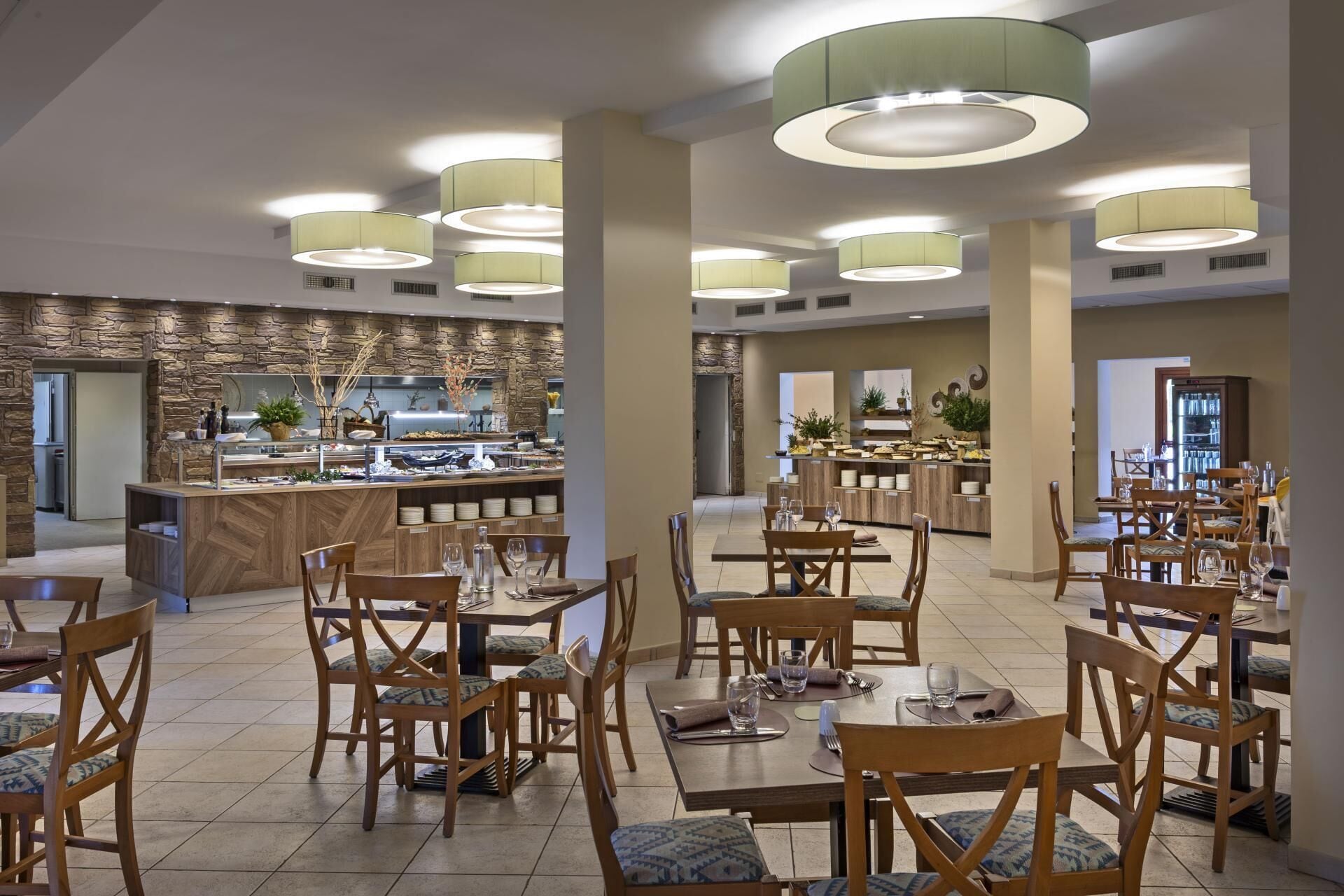 A modern dining area with wooden tables and chairs, a central buffet, and pendant lighting.