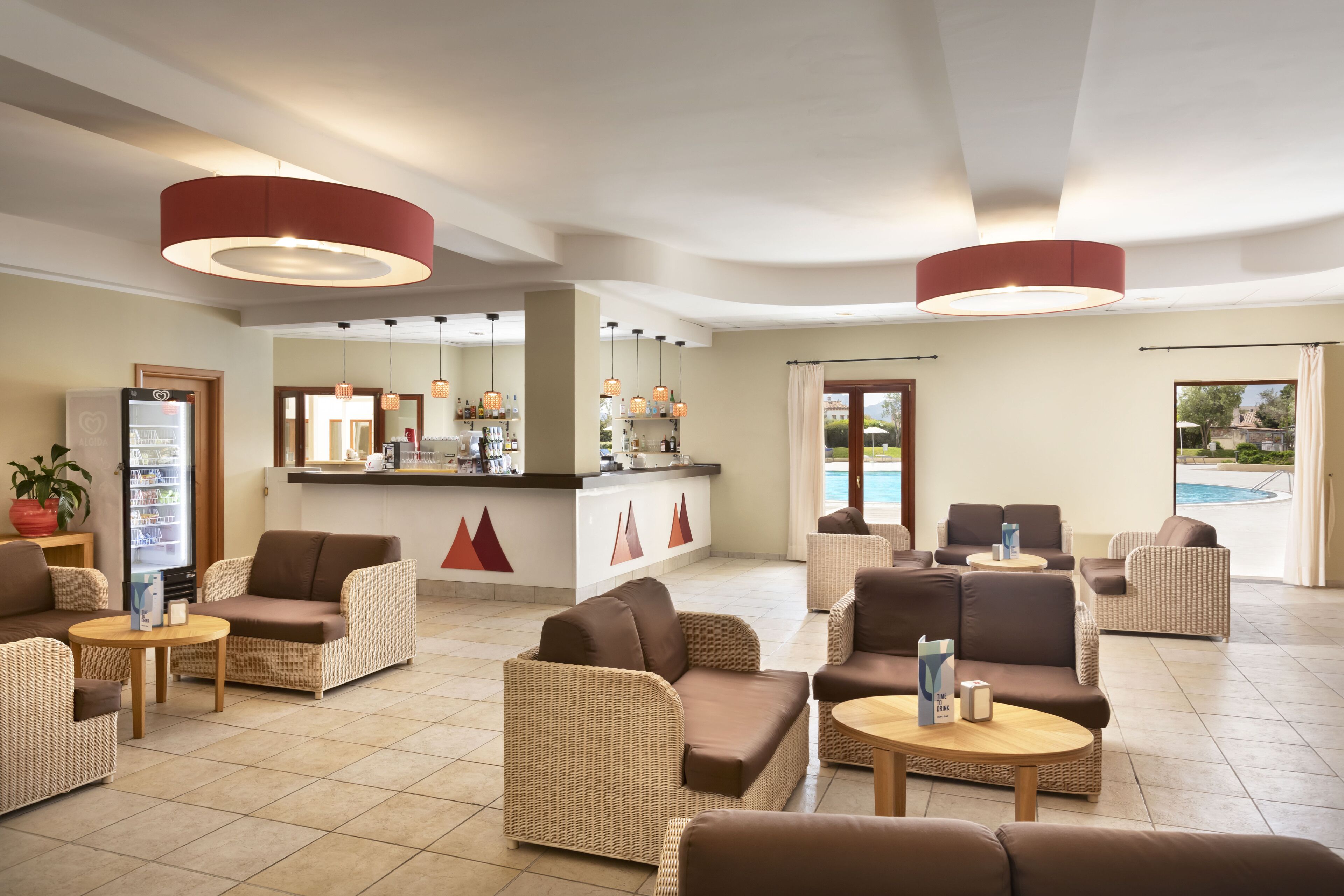 Eine großzügige Lobby mit Korbmöbeln, einem Empfangstresen und Blick auf einen Pool.