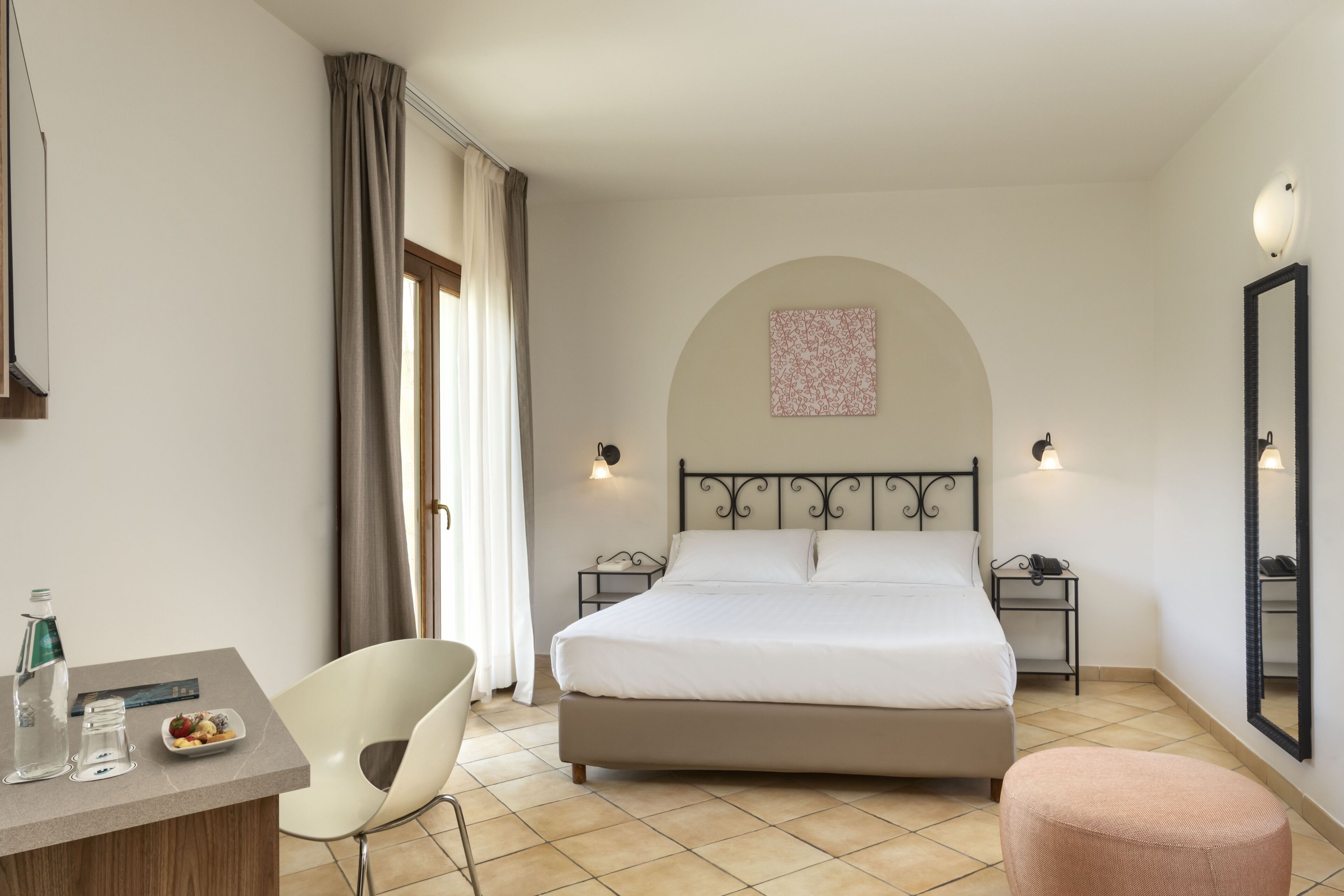 A bedroom with a bed, bedside tables, a chair, a desk, and a mirror.