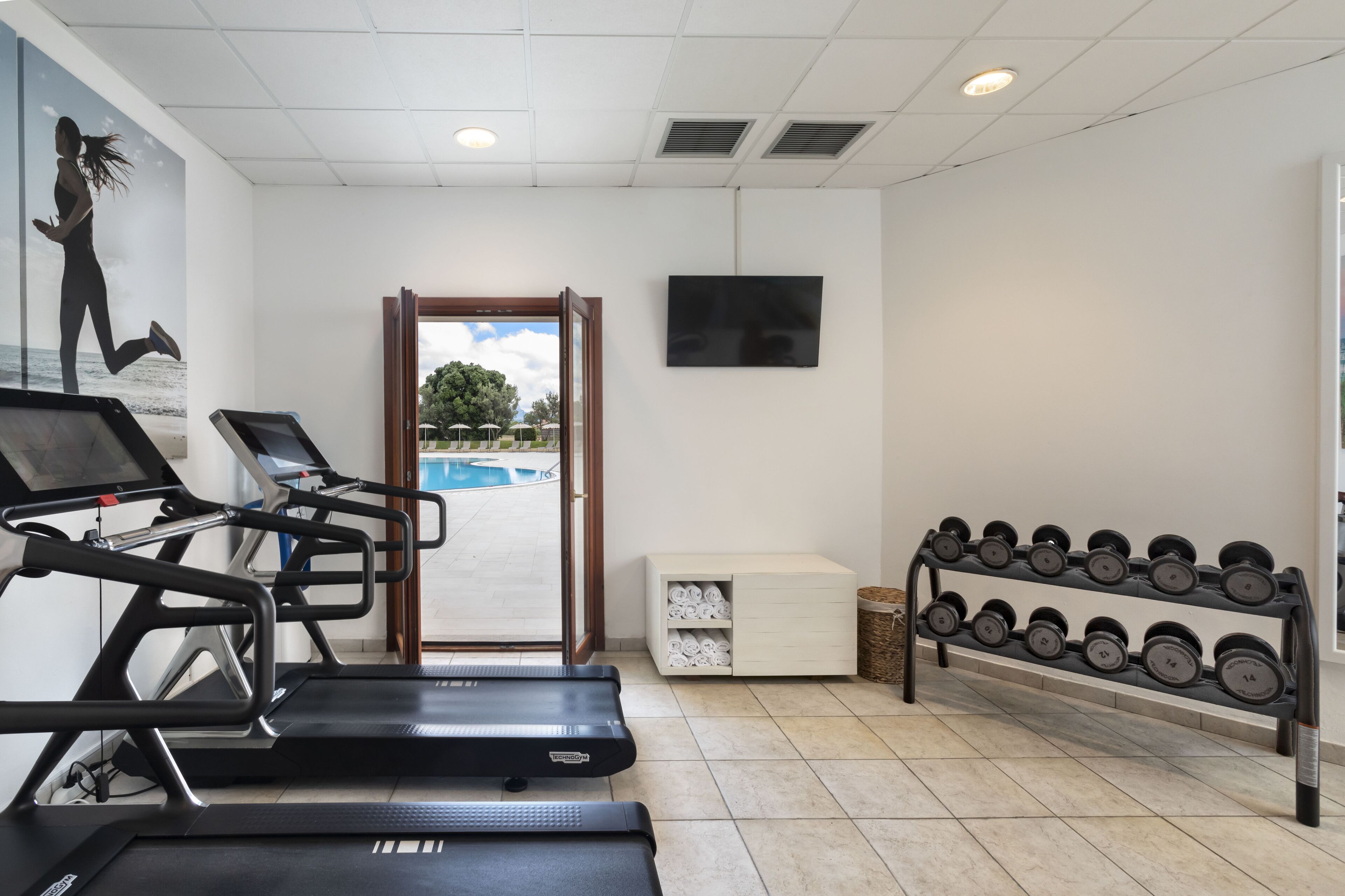 A fitness room with treadmills, a dumbbell rack, and a pool view.