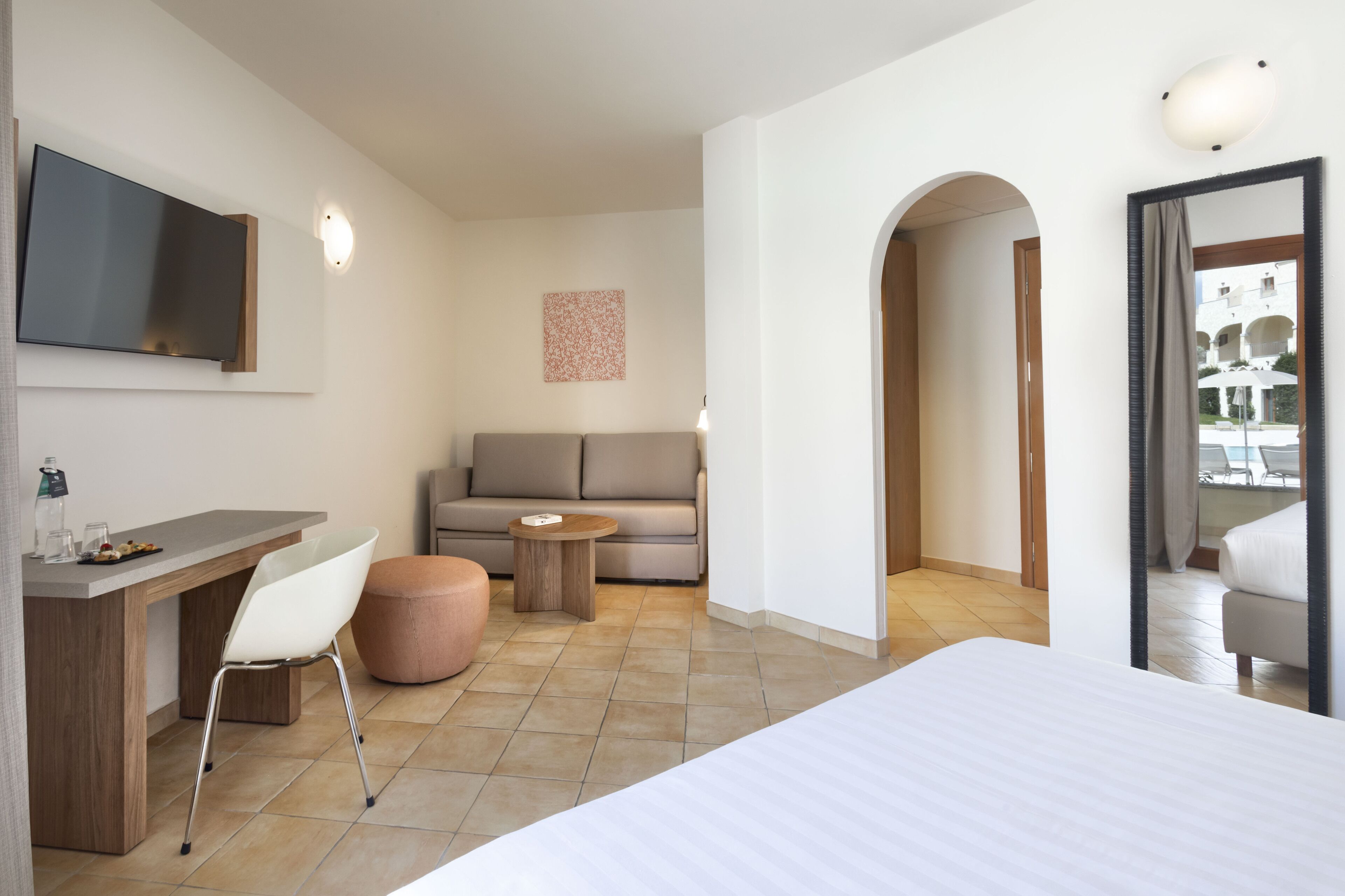 Ein modernes Hotelzimmer mit einem Bett, einem Schreibtisch mit Stuhl, einer Couch, einem kleinen runden Tisch und einem an der Wand montierten Fernseher.