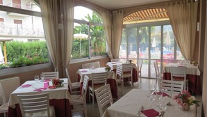 Um restaurante com mesas preparadas para refeições, grandes janelas e vista para o exterior.