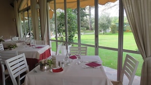 A restaurant with tables set for dining, large windows, and a view of a garden. - La Quiete Park Hotel (Manerba del Garda)