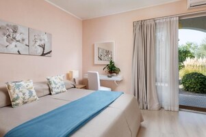 A hotel room with a bed, a desk, a chair, a window with curtains, and artwork on the walls.